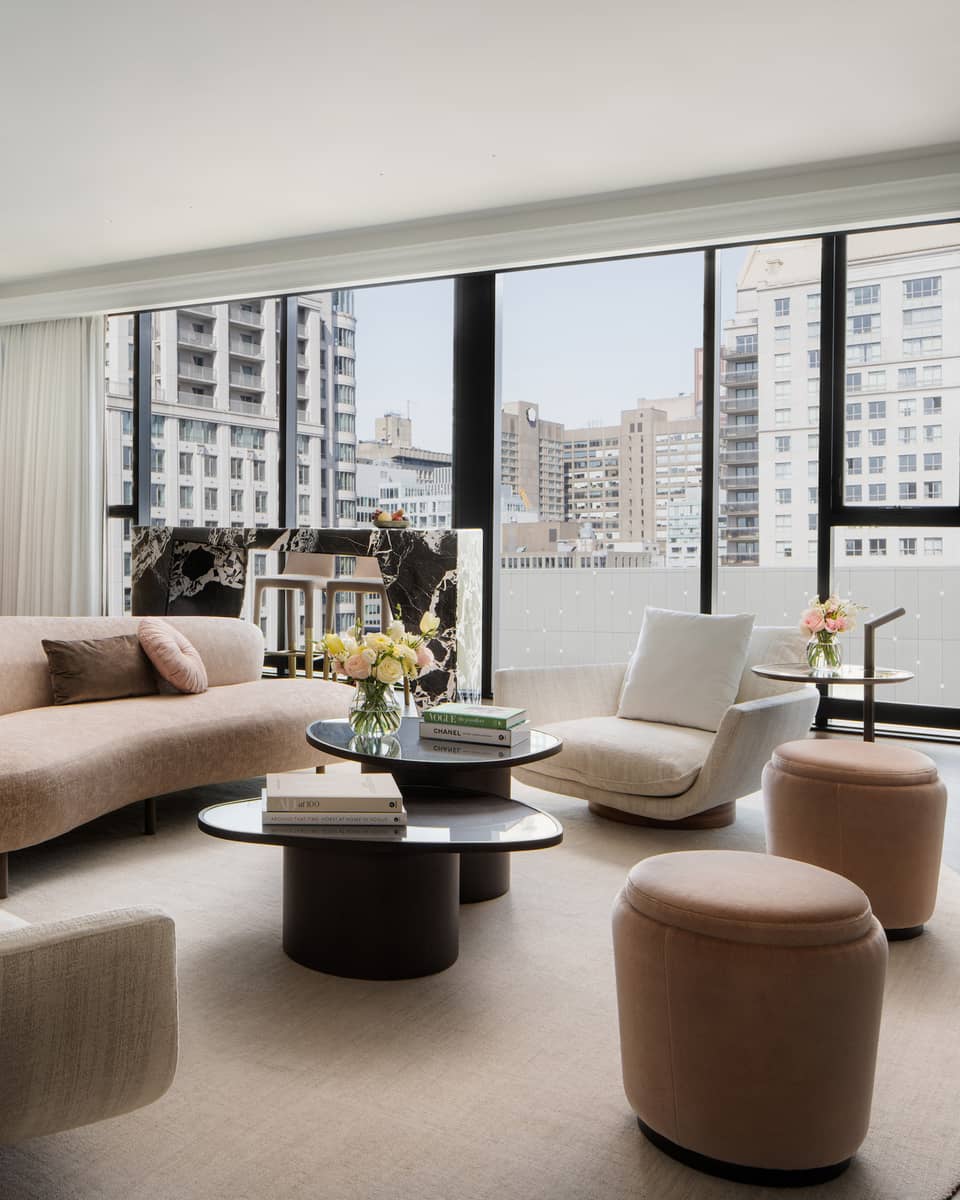Hotel suite living room with beige curved sofa, two modern armchairs and walk-out balcony