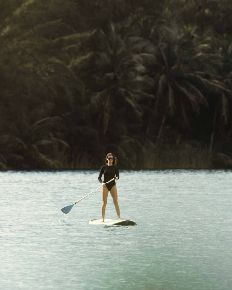 A person on a stand-up paddleboard on the water with lush trees in the background