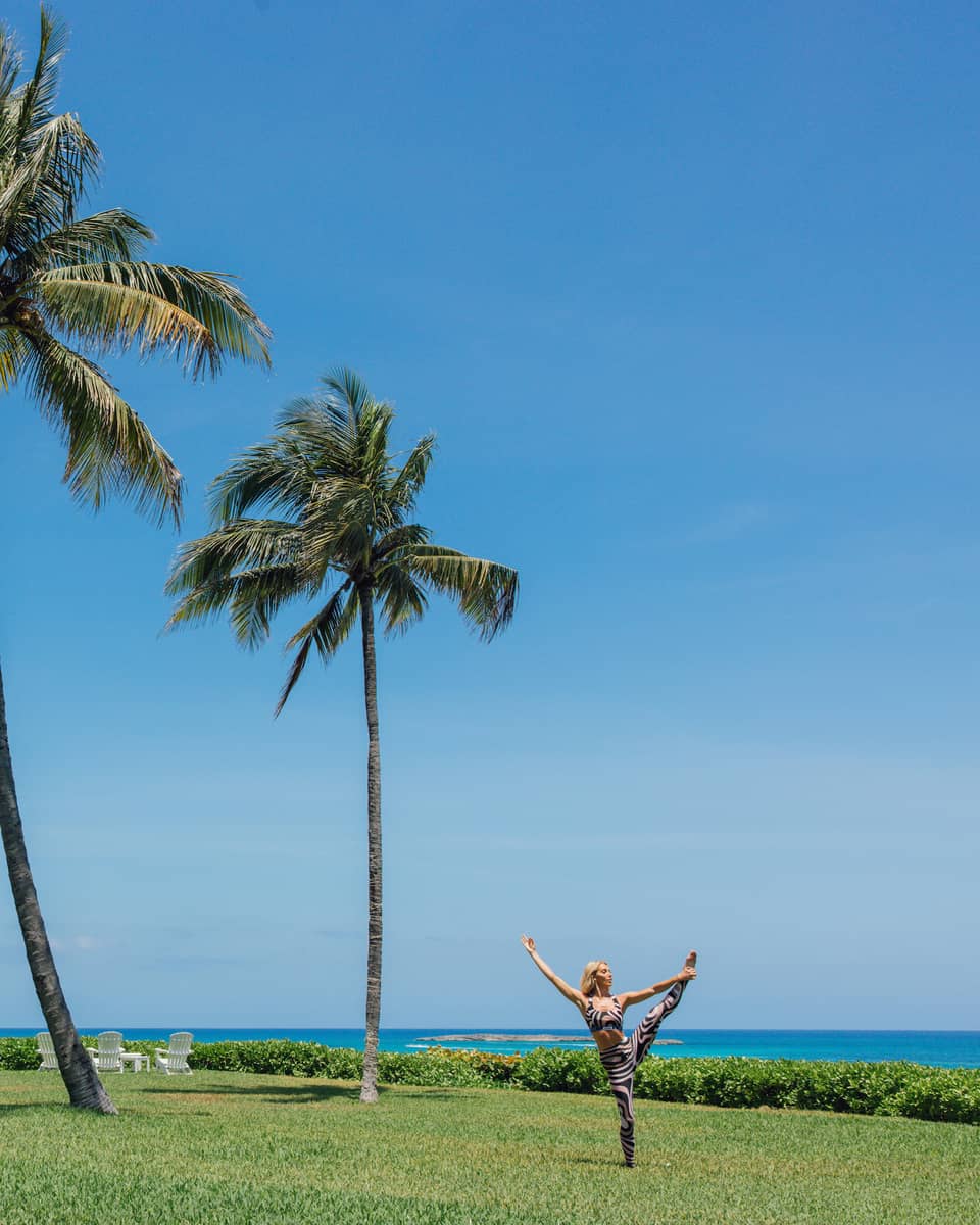 A person doing a yoga pose outside near the ocean and palm trees