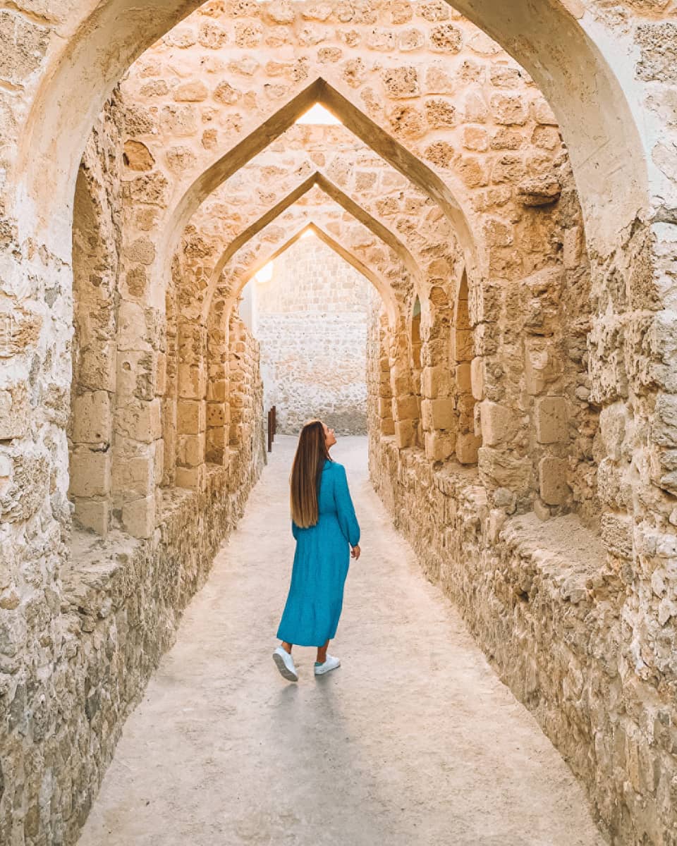 A woman stands underneath a stone pathway.