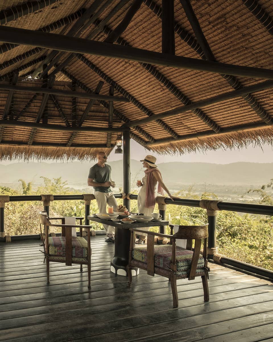 A couple sitting on a wooden deck overlooking green brush, Land Rover sitting nearby 