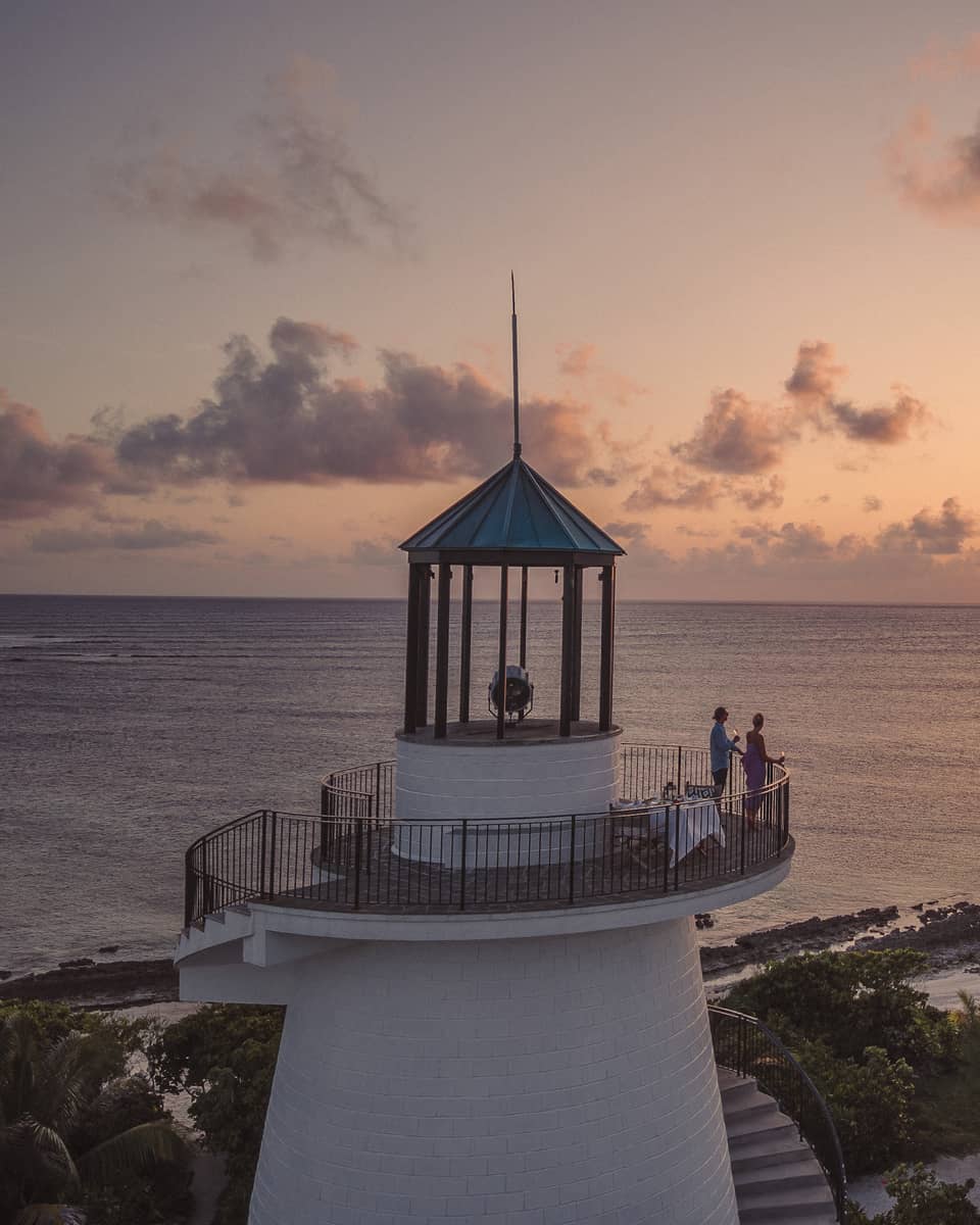 Long view of two people on a beach lighthouse balcony, enjoying the sunset over the ocean, distant silhouette of birds. 