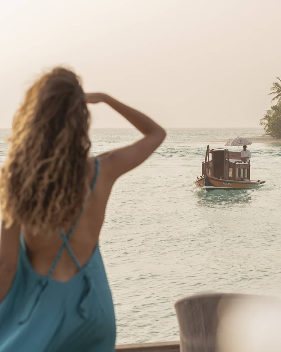 Person in blue dress shields eyes as boat travels toward shore