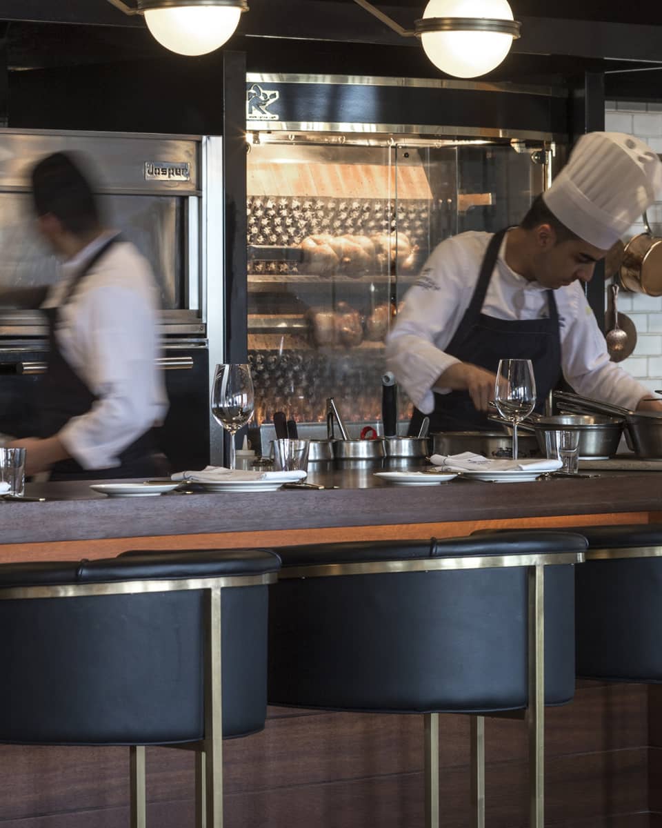 Chefs working behind a counter with black-and-gold stools in the foreground