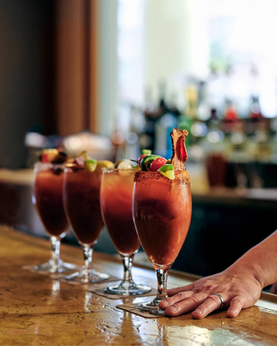 ,A bartender serves up four bloody marys at a bar