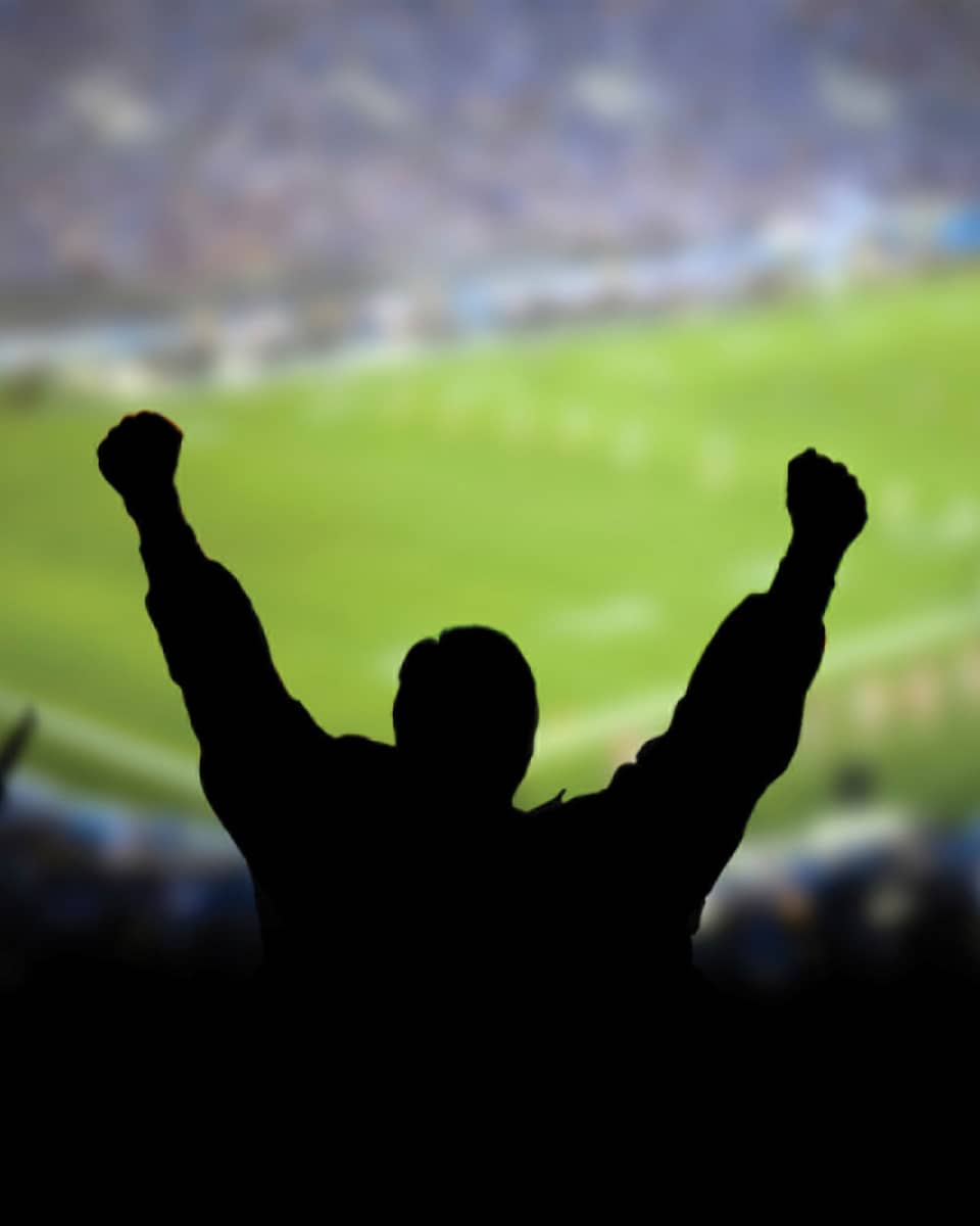 A silhouette of a person cheering at a football stadium.