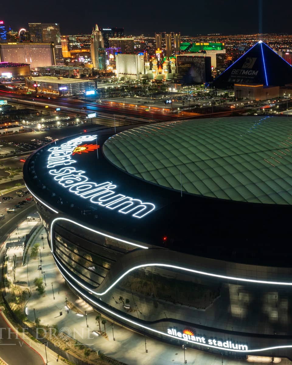 A nighttime, birds-eye view of a large sports stadium, with other tall buildings and lights around it.