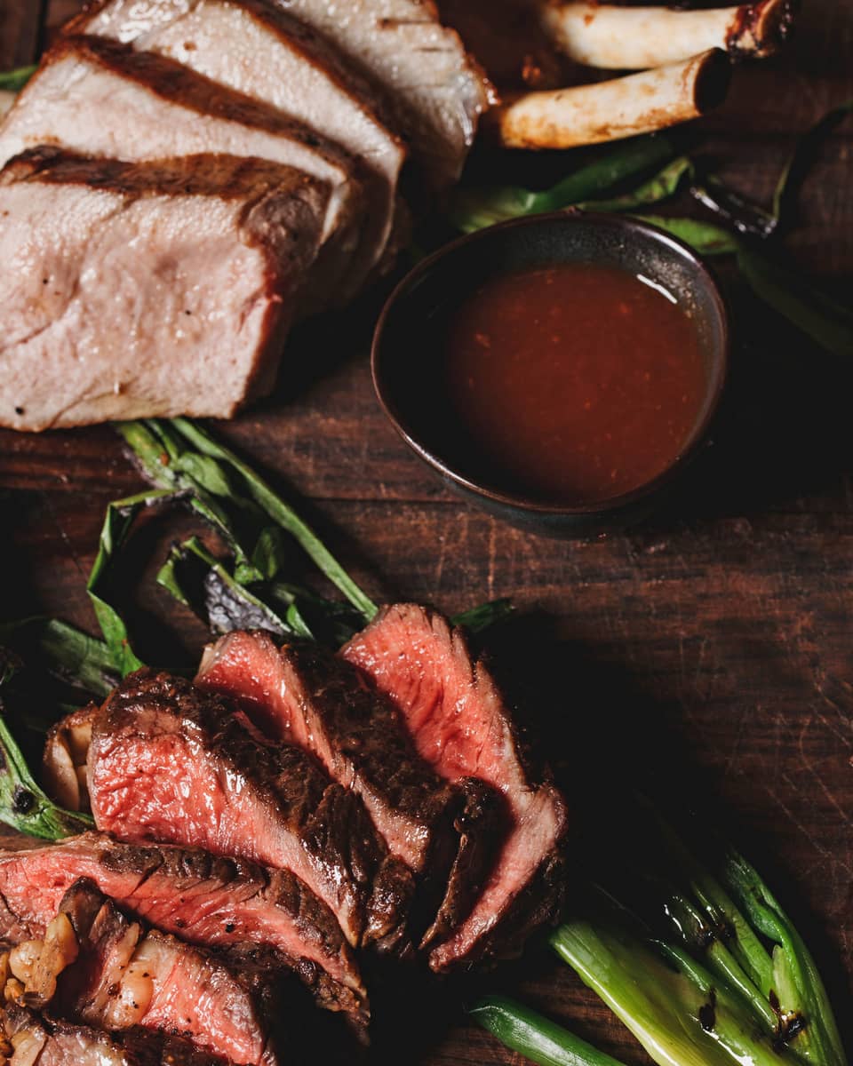 A aerial view of the La Hiki Steak over green onions with a red sauce on the side