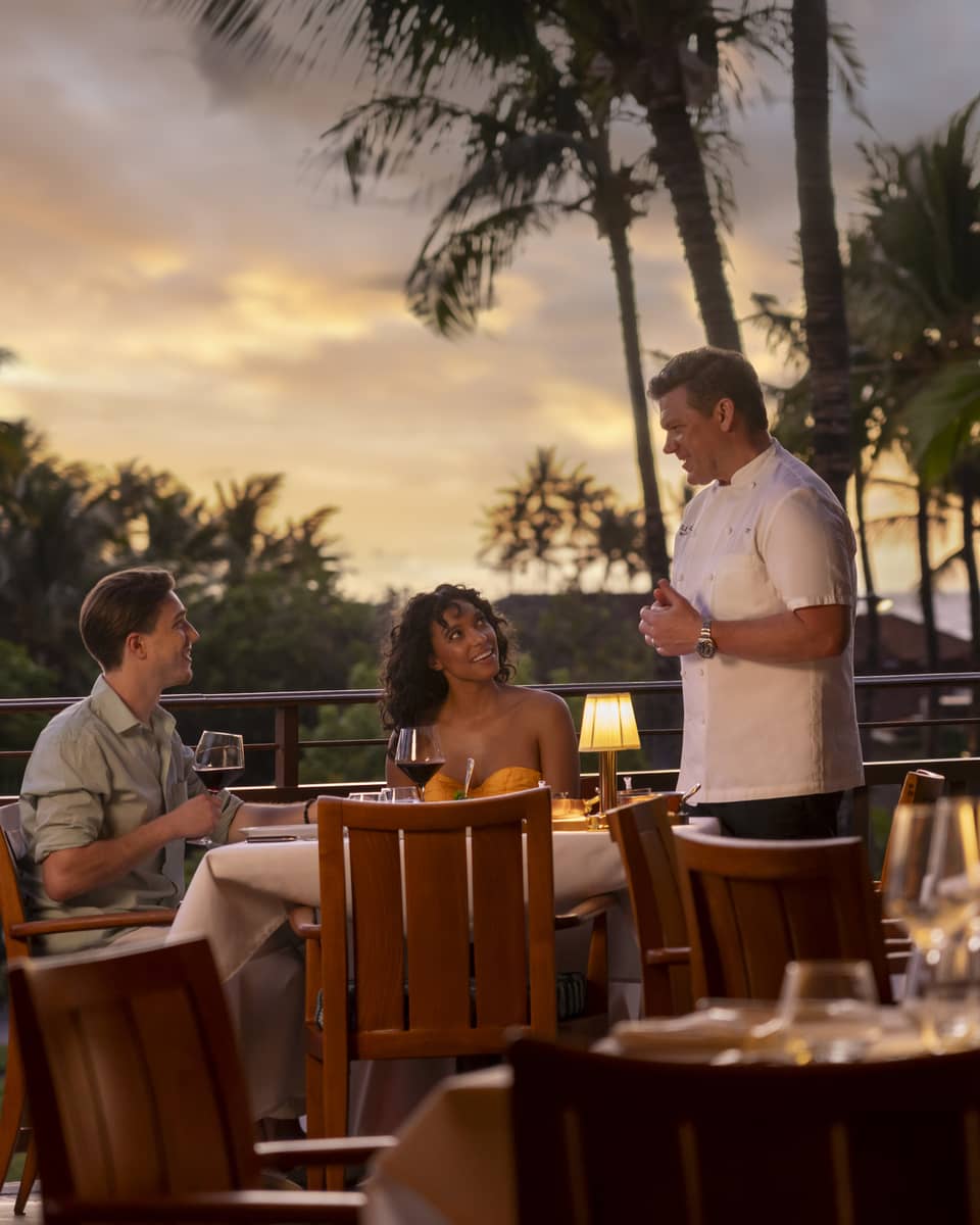 Chef Tyler Florence speaks to man and woman dining at outdoor Miller and Lux Hualalai restaurant
