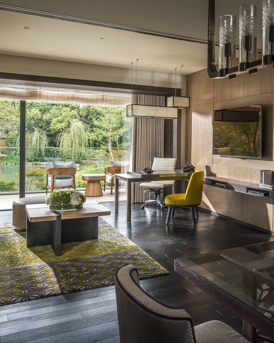 Long glass dining table under chandelier by living room, open wall to sunny patio
