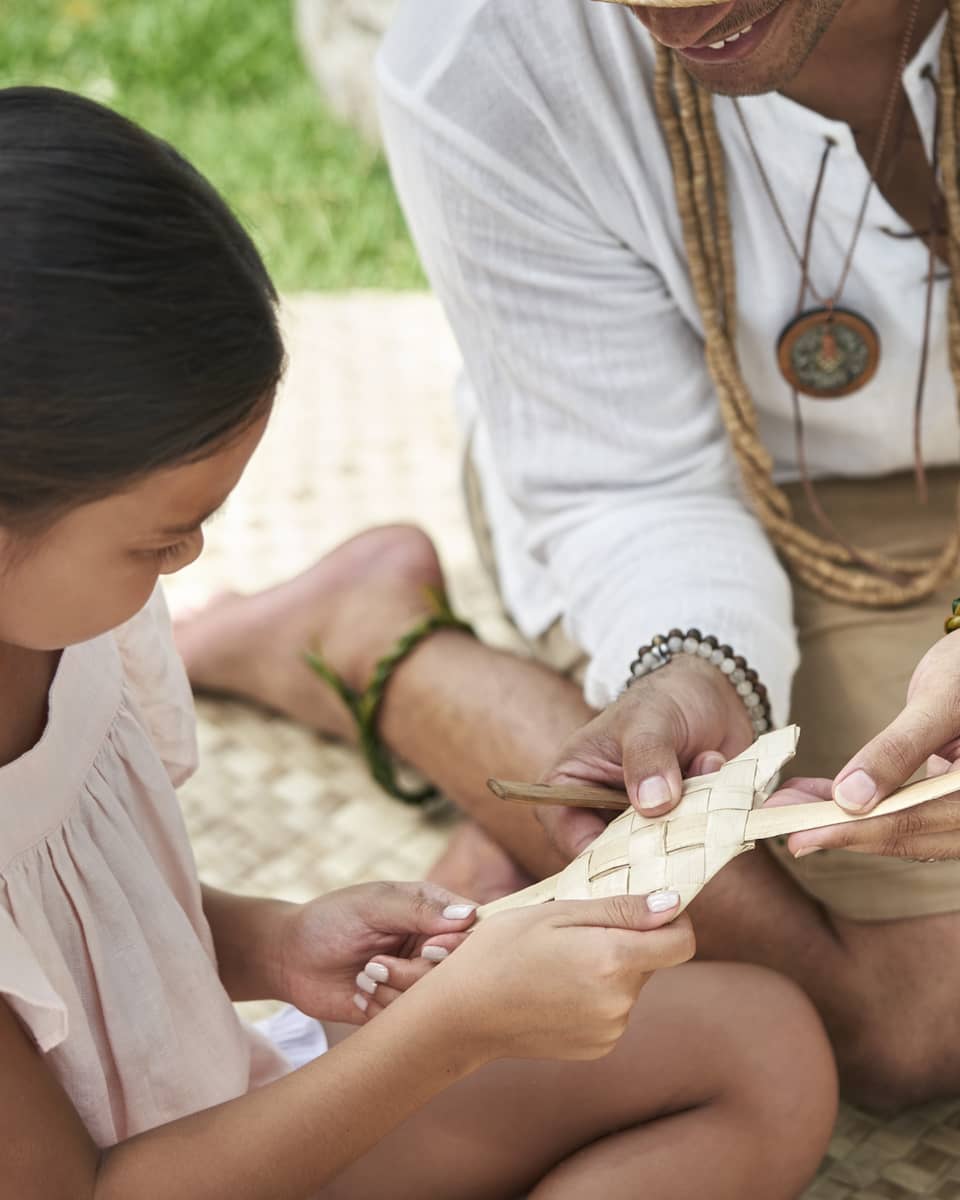 An adult shows a young girl how to weave a basket