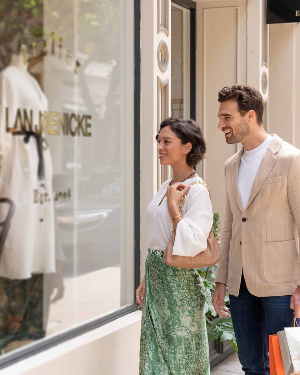Two people smiling while window shopping in front of a boutique store.