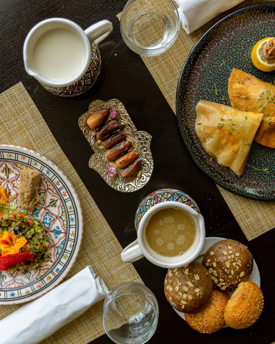 Two plates of international dishes, served with sides of dates and rolls