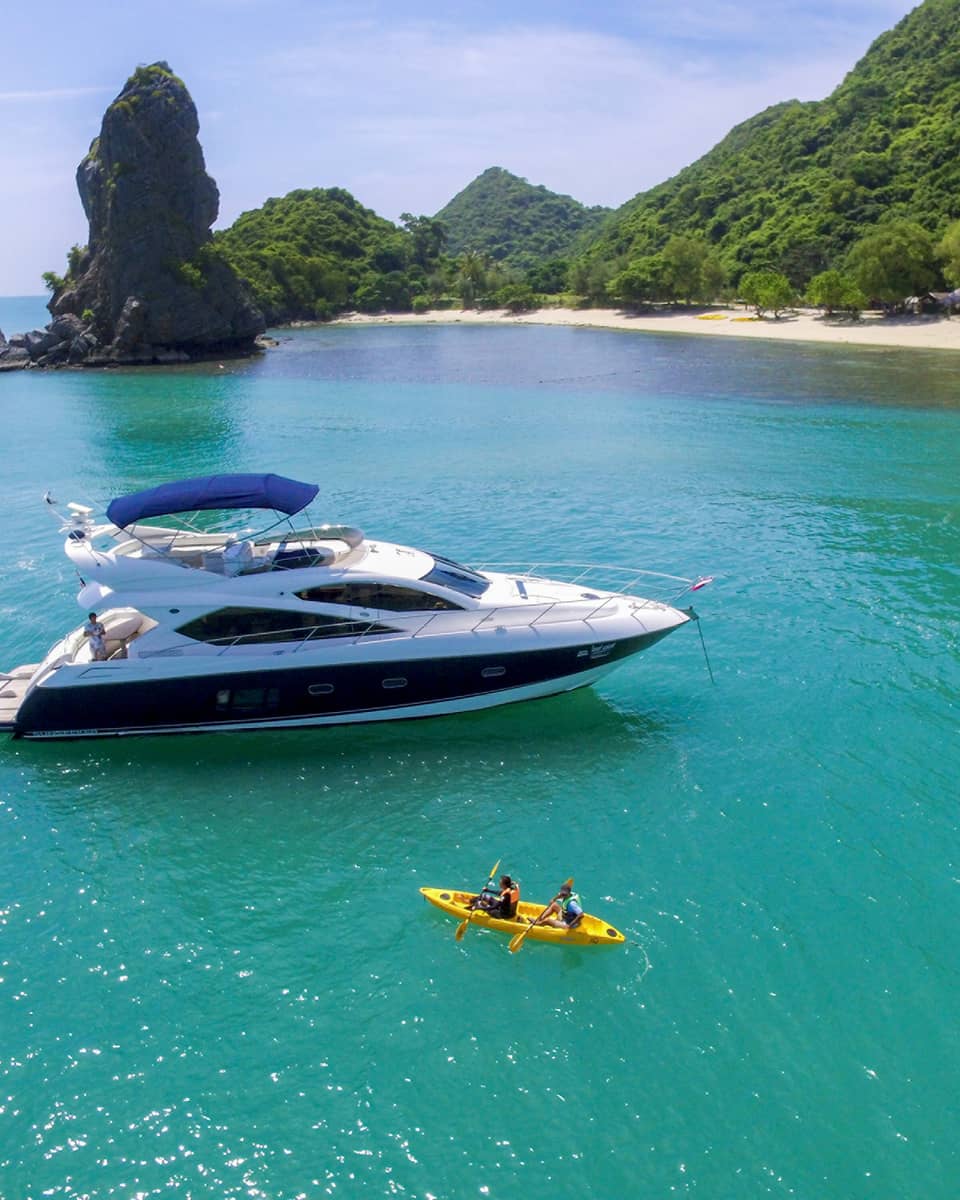 Two people in yellow kayak in front of large white yacht by island in blue ocean