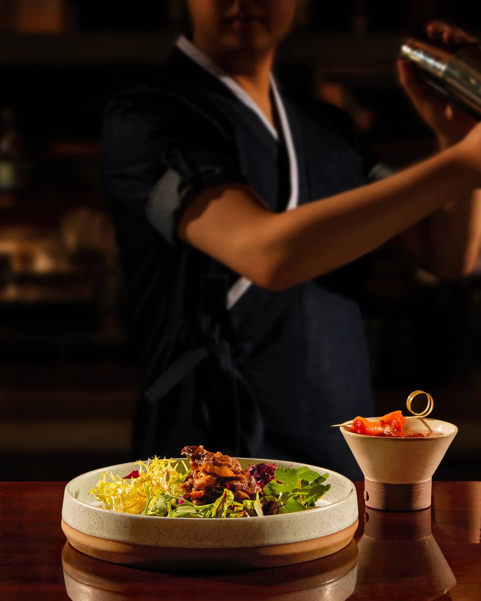 Bartender shaking a cocktail, bar bites at the forefront