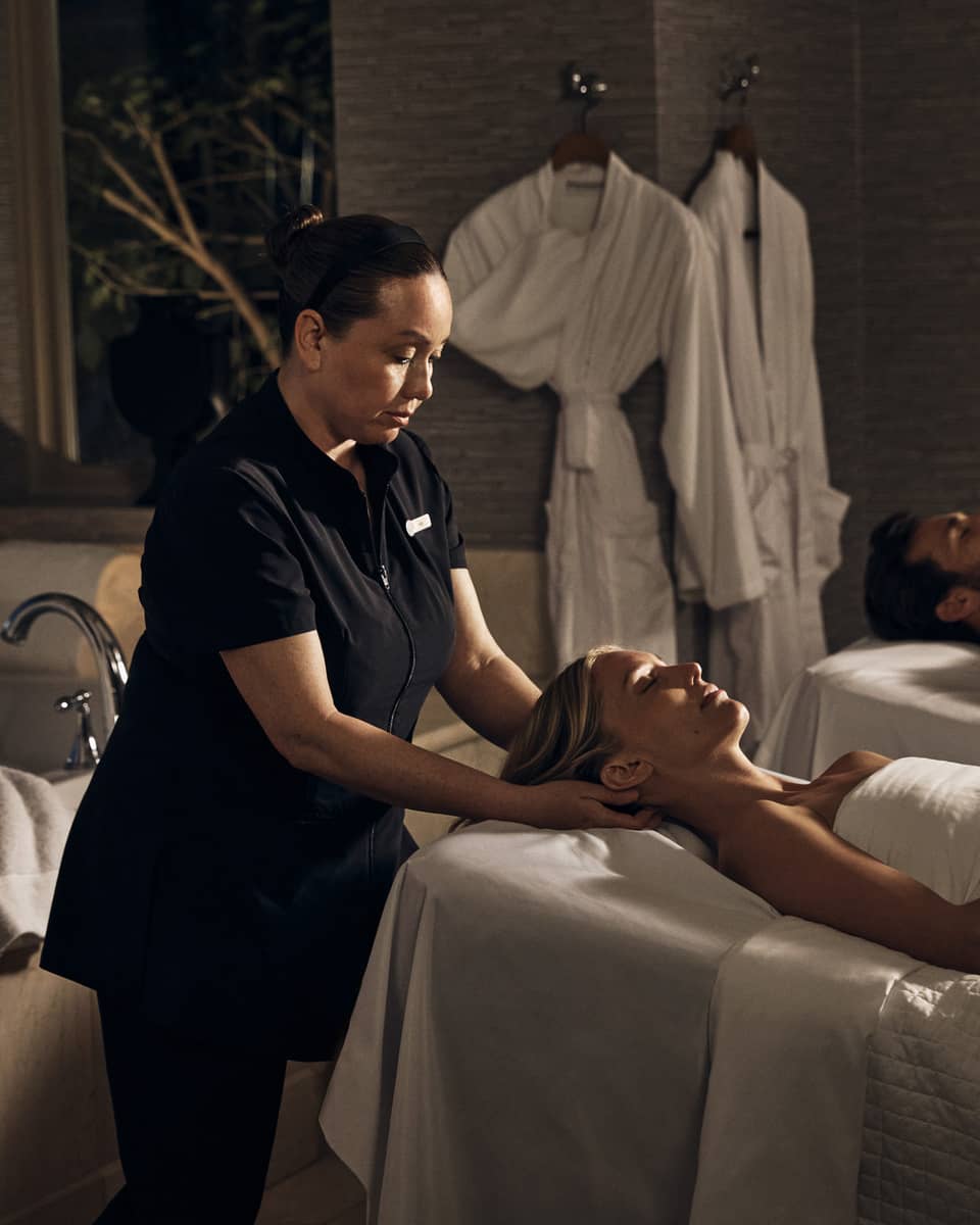 Two guests laying on massage tables in a room with a spa tub.