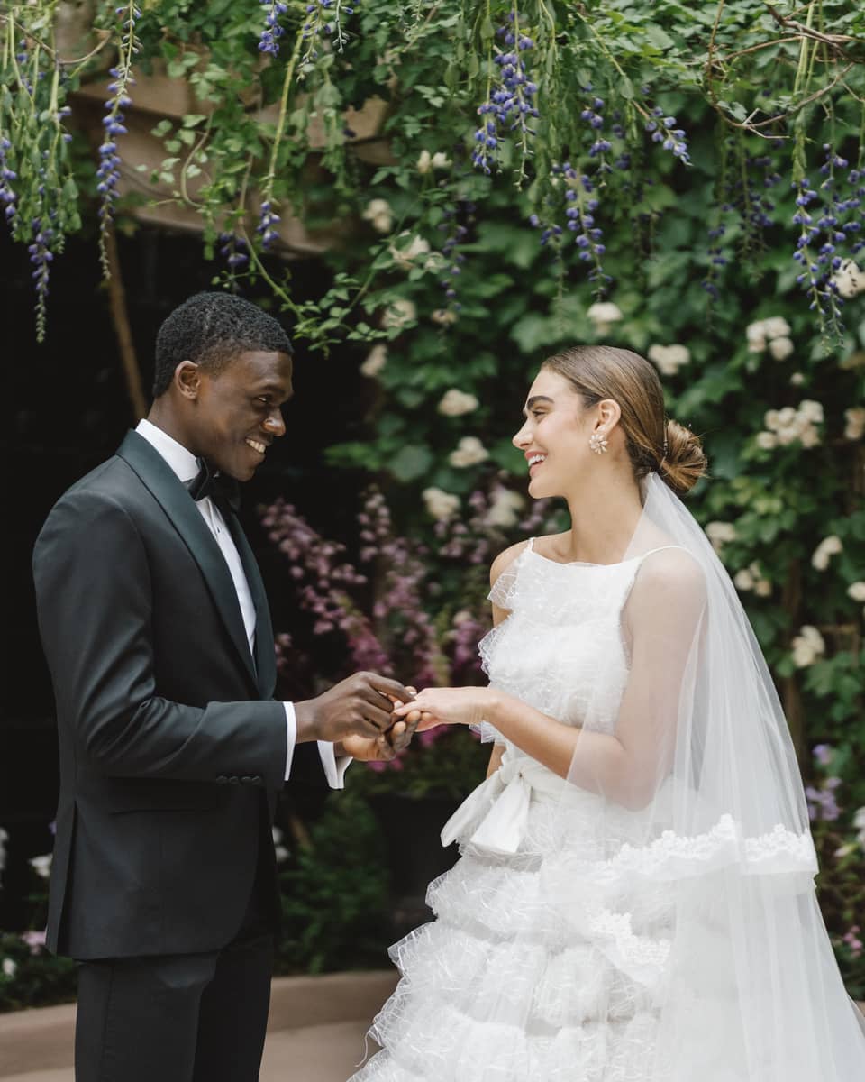 A bride and groom holding hands surrounded by brick walls and flowers.
