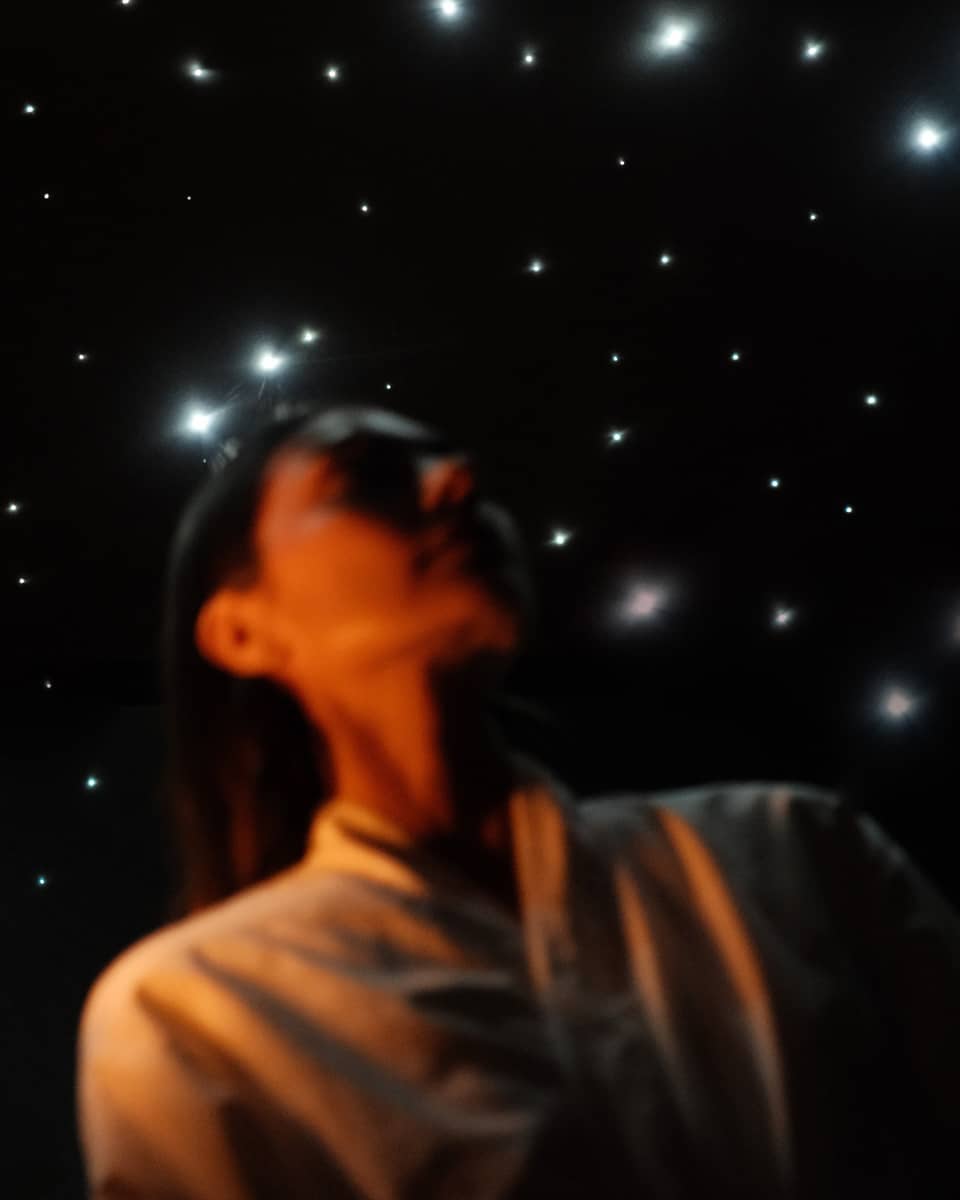 Guest wearing white spa robe stands in front of a ceiling lit to resemble a night sky filled with stars