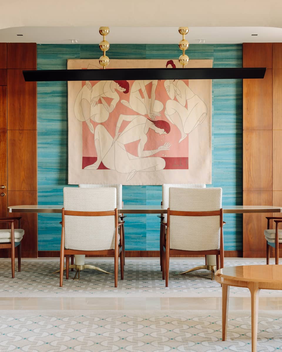 Elegant dining area with a long table, white chairs, colorful wall art and wood-paneled walls framed by an arched entryway.