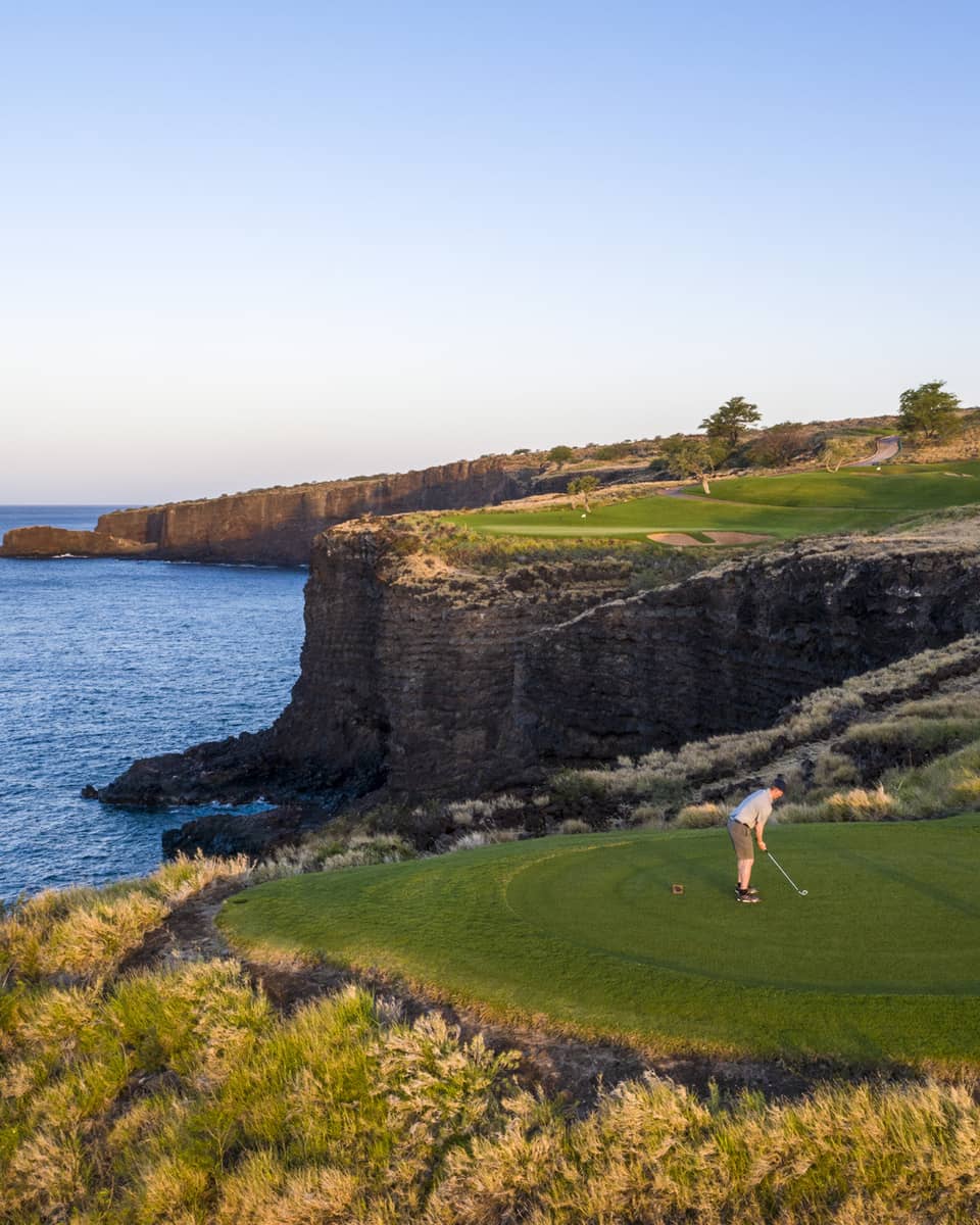Two golfers at the 12th-hole tee at Manele Golf Course at Four Seasons Resort Lanai, cliffs and ocean in background
