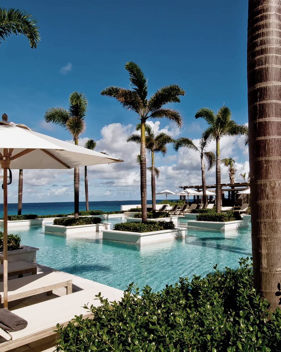 Aleta Pool with white potted palms, surrounded by white patio chairs, umbrellas, ocean views 
