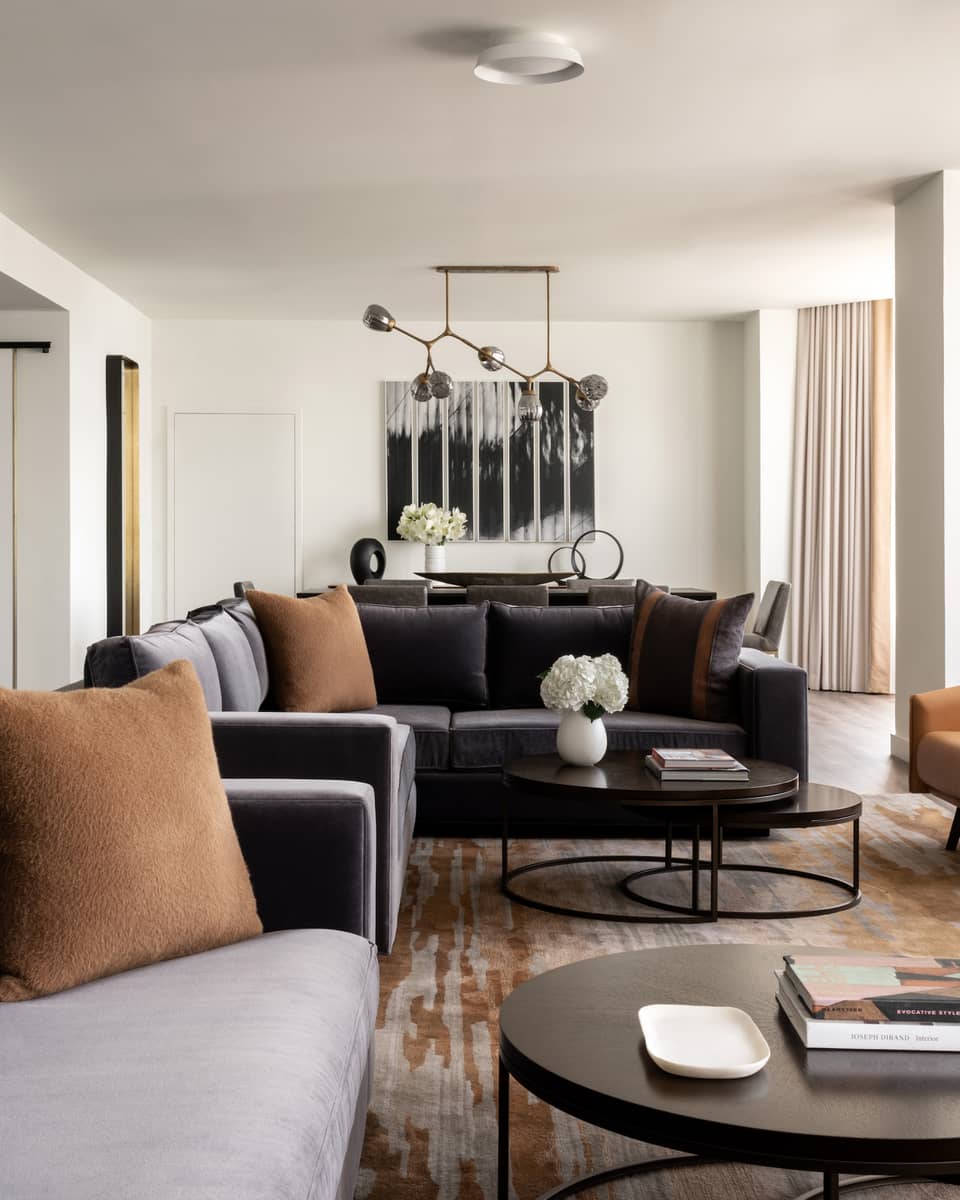 Living room with two grey-blue velvet sofas, tan leather arm chairs, round metal coffee table