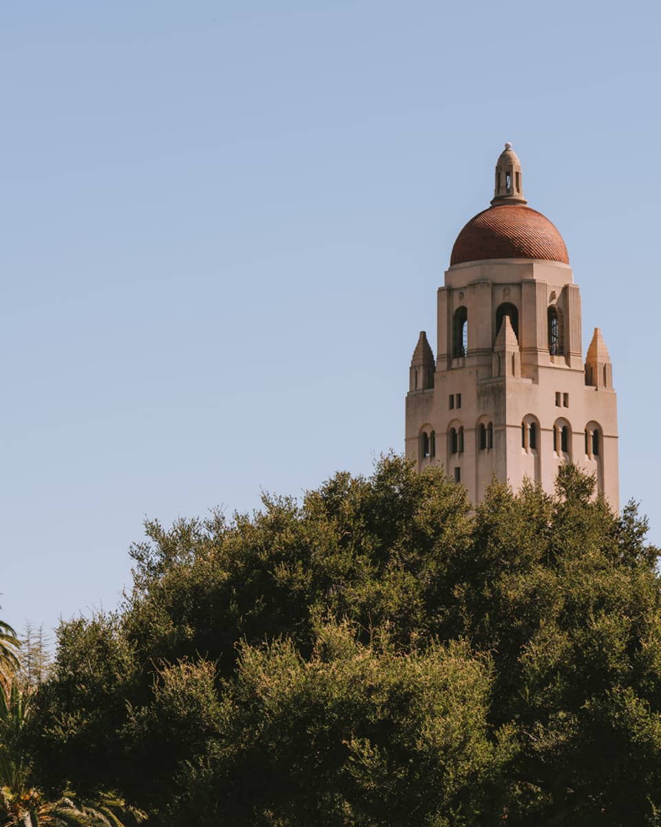 The top of a beige building with many trees in front of it.