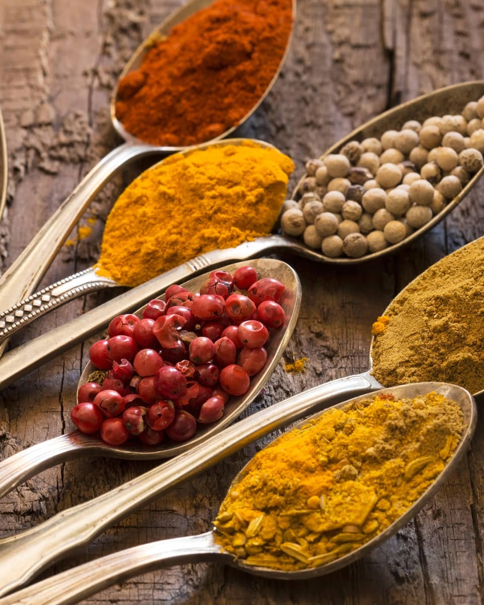 Seven silver spoons filled with various spices.
