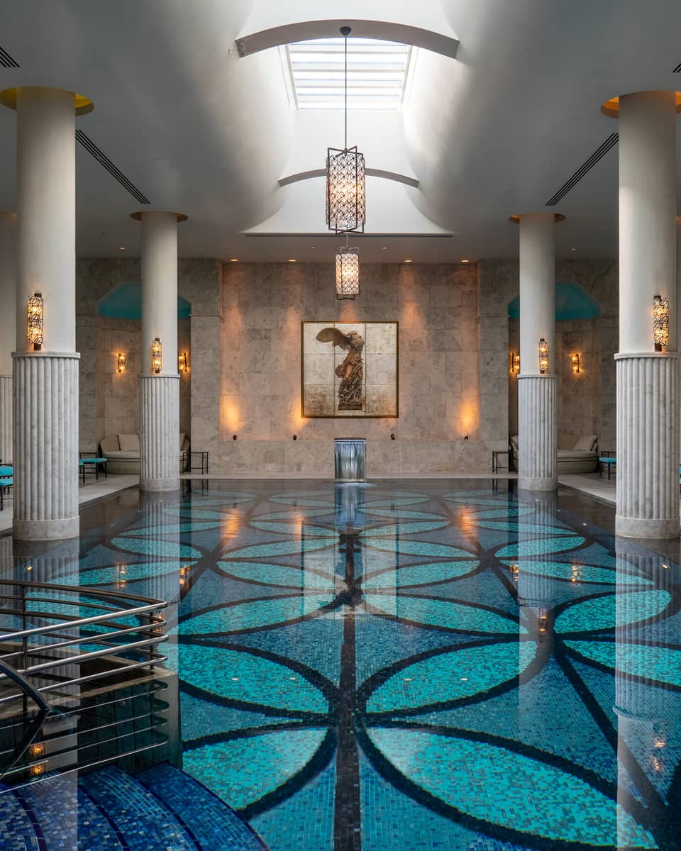 Indoor pool with blue-patterned floor, white up-lit columns and skylight