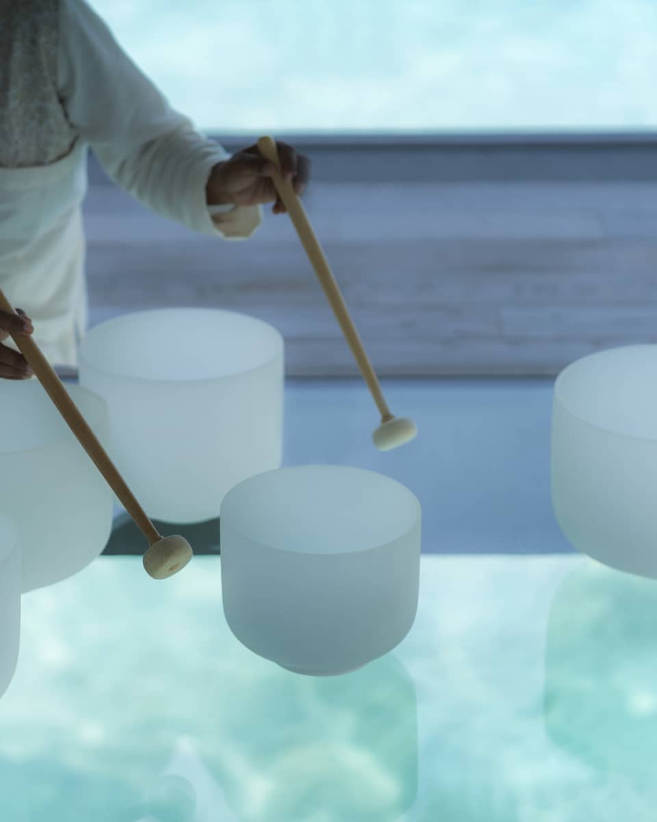 Spa staff plays various white crystal bowls with wood mallets during sound healing session