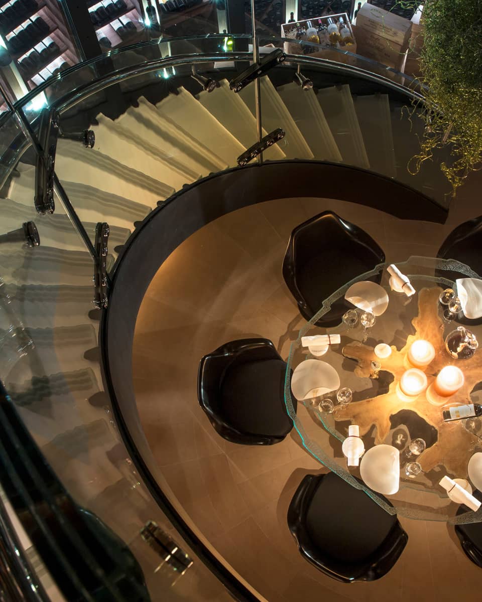 Aerial view of round glass candle-lit dining table, chairs from spiral staircase