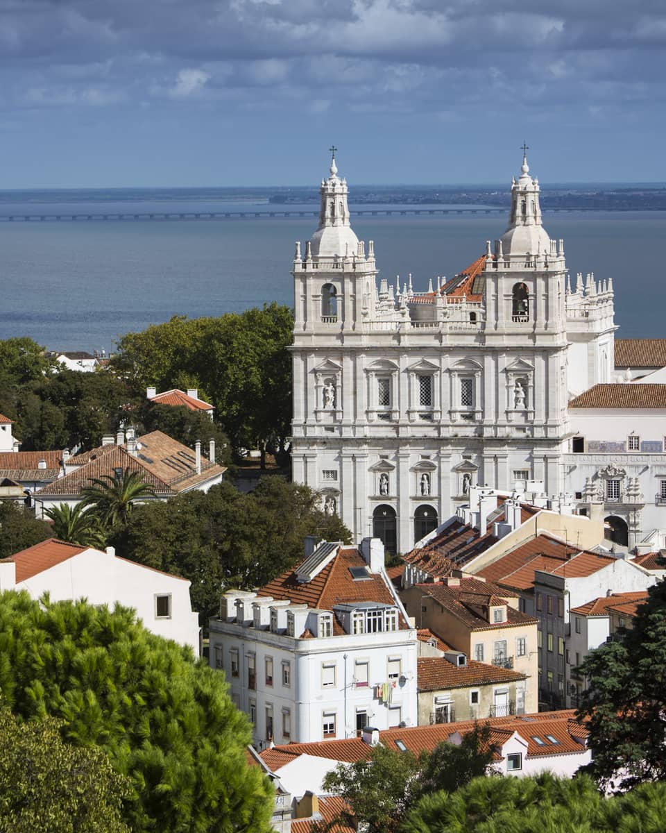 White cathedrals, houses and rooftops in Lisbon, ocean in background
