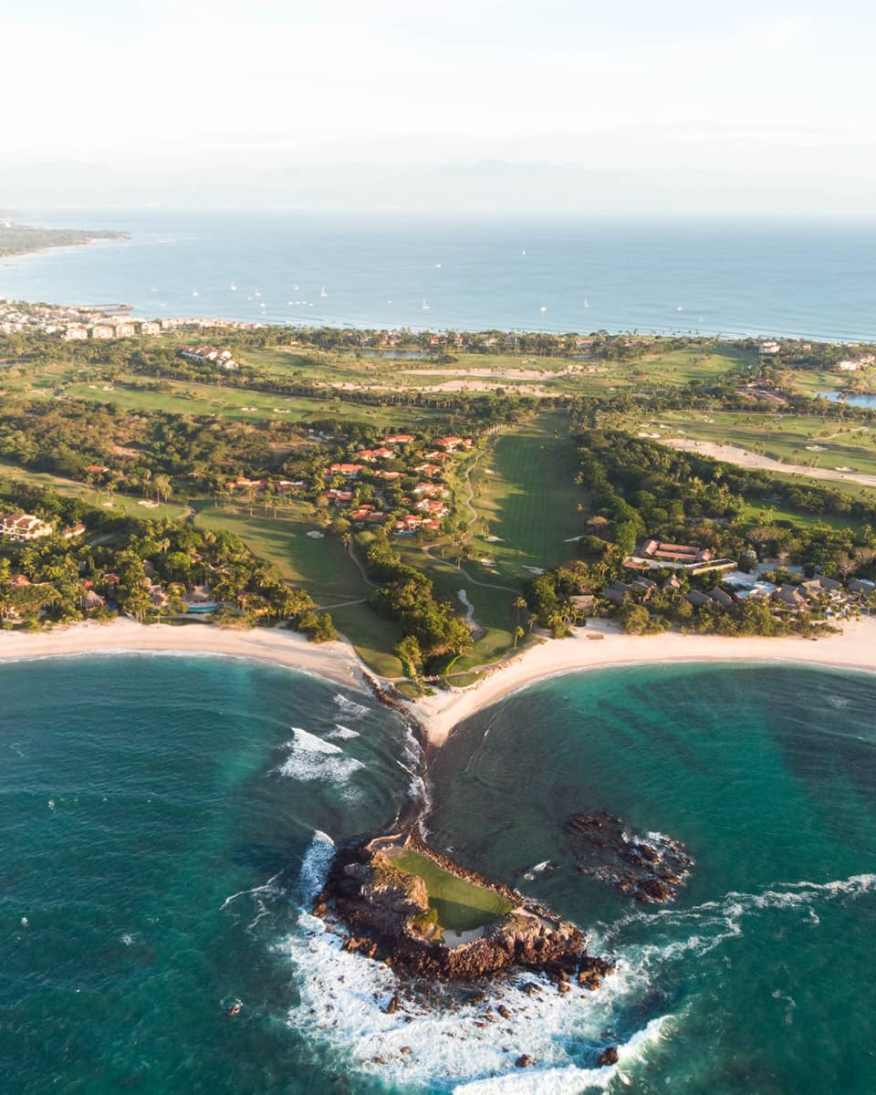 A coastline with deep blue water running up against sand and plants.