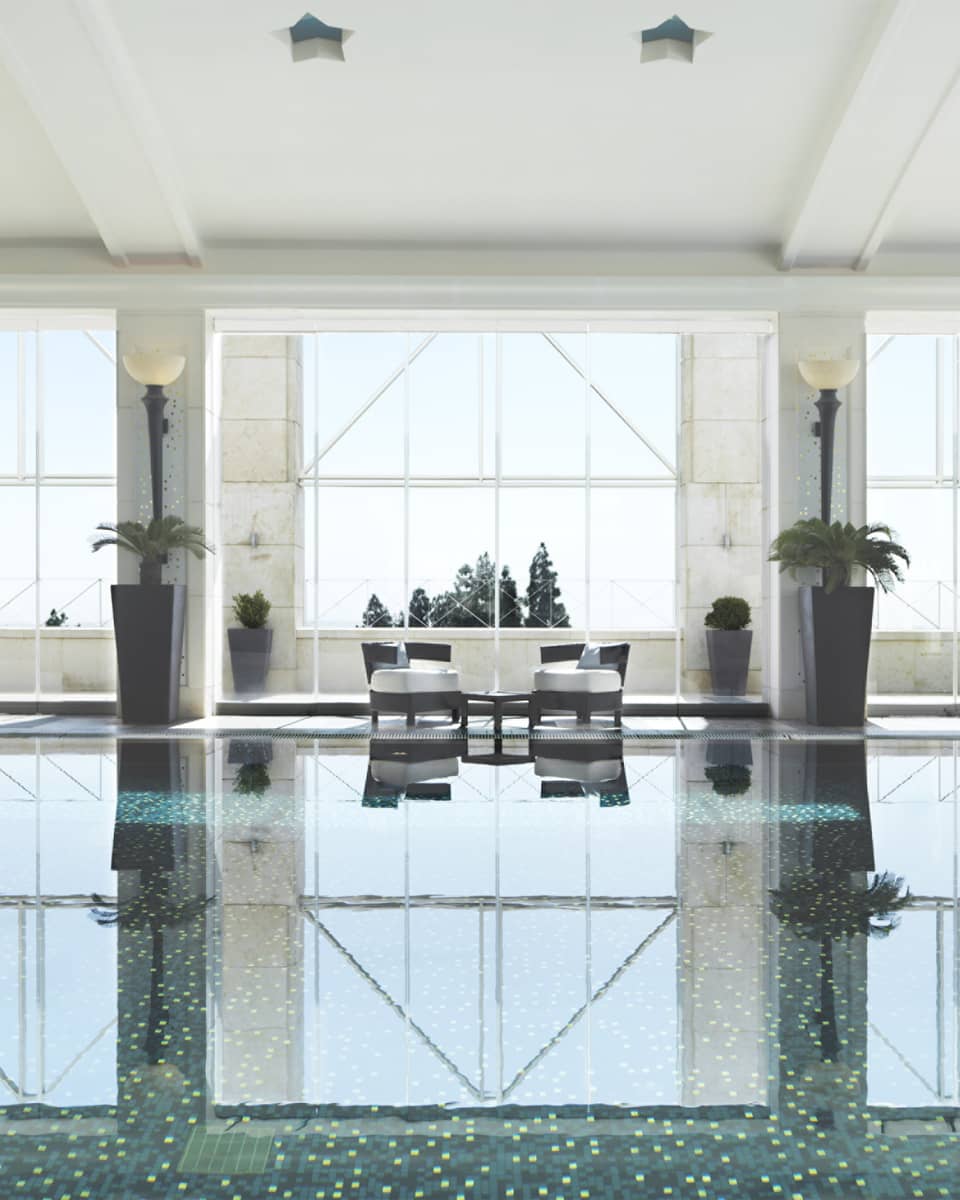 Indoor swimming pool reflecting light of three tall windows, white walls and pool chairs 