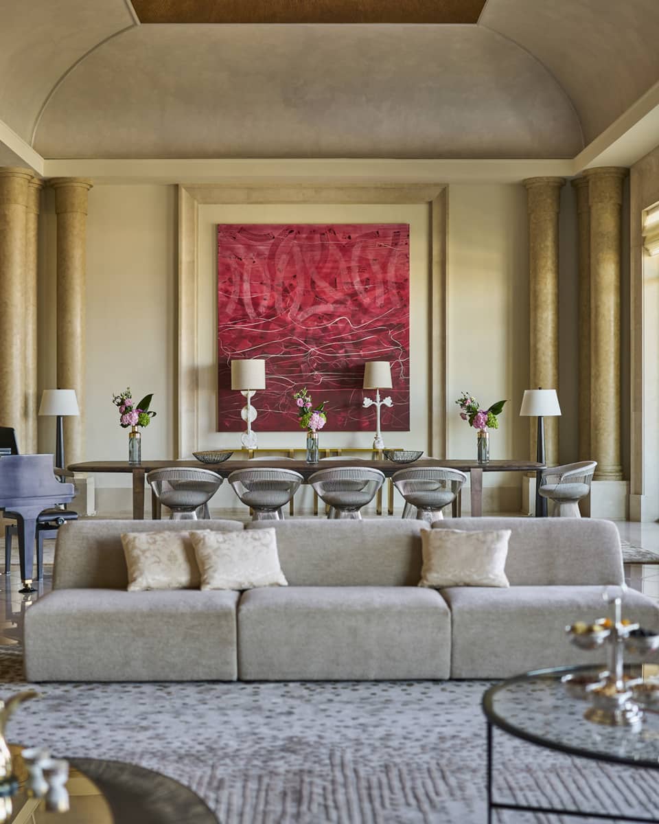 Grand hotel suite living room with pillars, a modern sofa and a large dining table set next to red artwork