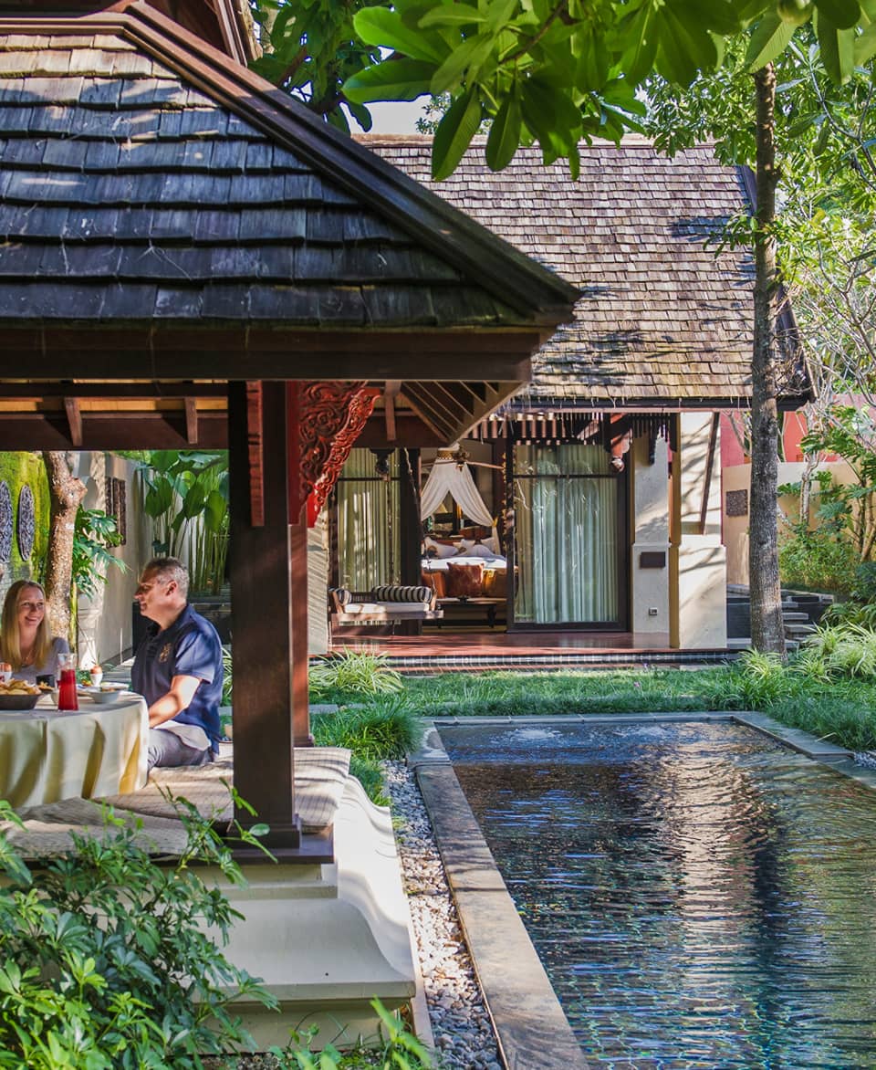 Hotel staff serve couple under dining gazebo by pond 