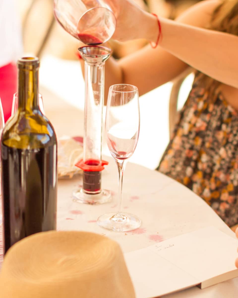 Close-up of man and woman pouring wine into glass decanter, open wine bottles on table