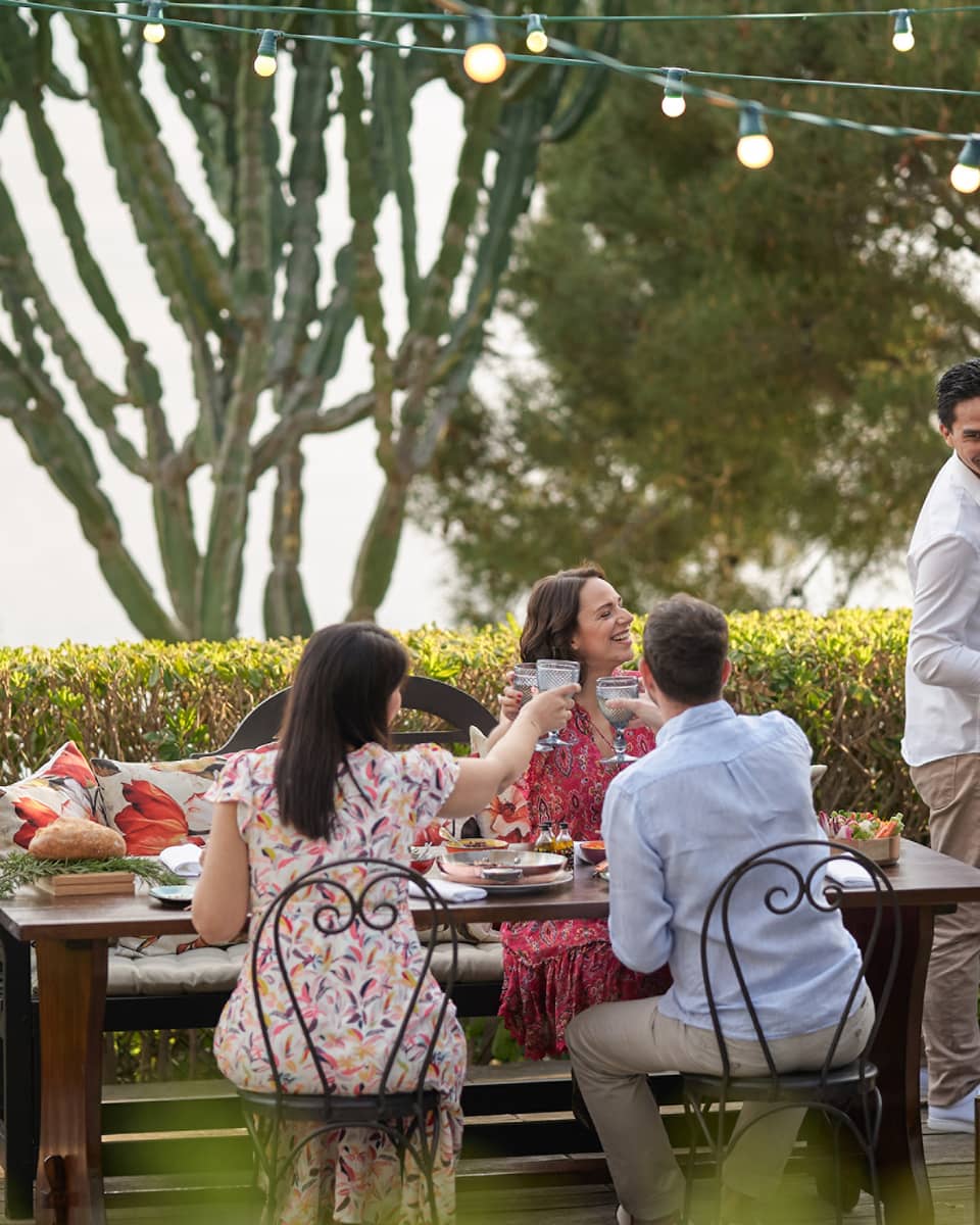 A group of four people grilling food outside at a large table while wearing nice beach clothes.