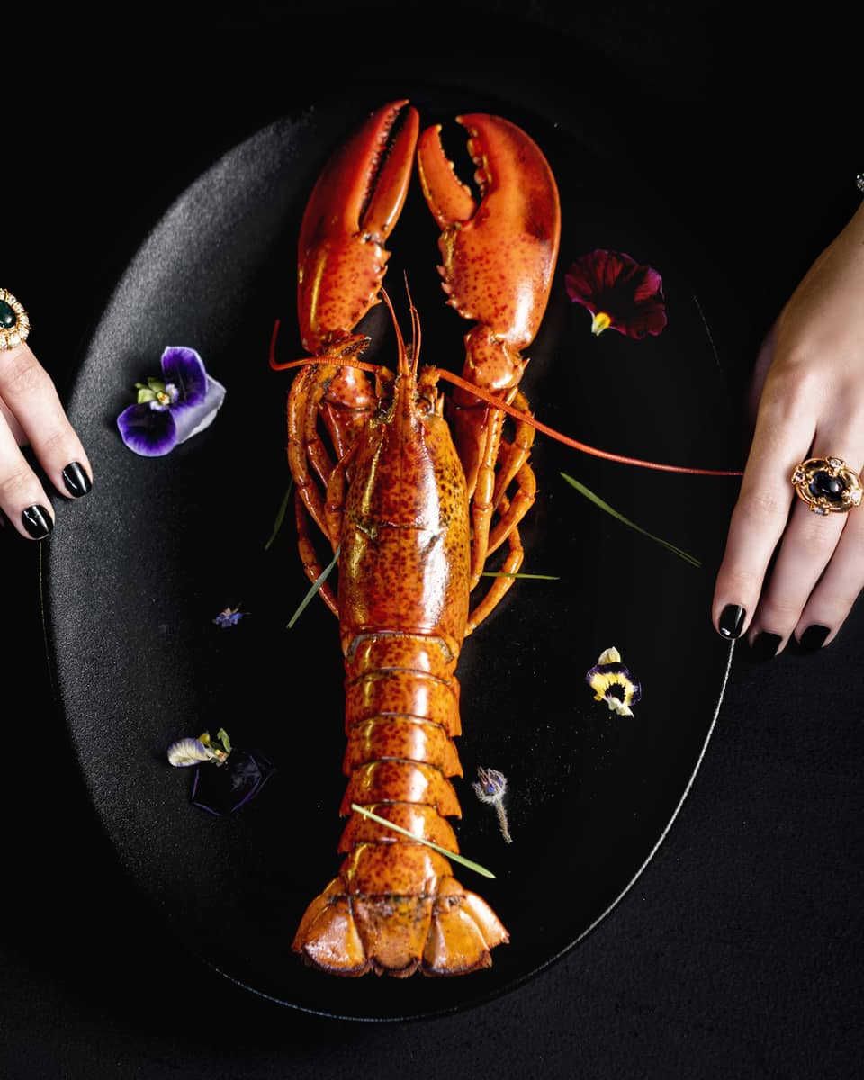 Whole lobster plated vertically on black plate with garnish