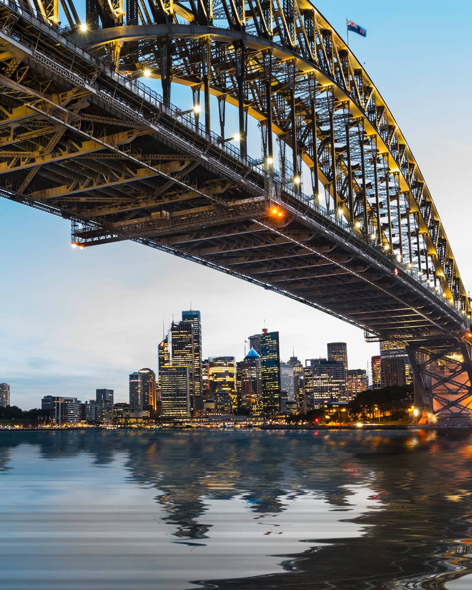 View from under bridge to Sydney waterfront skyline, lights at dusk