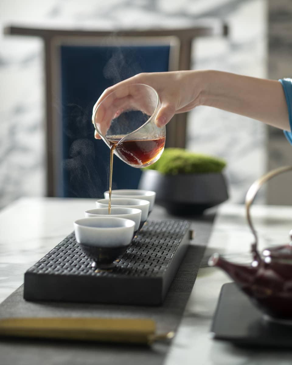Woman's hand pours tea into mugs for traditional tea ceremony