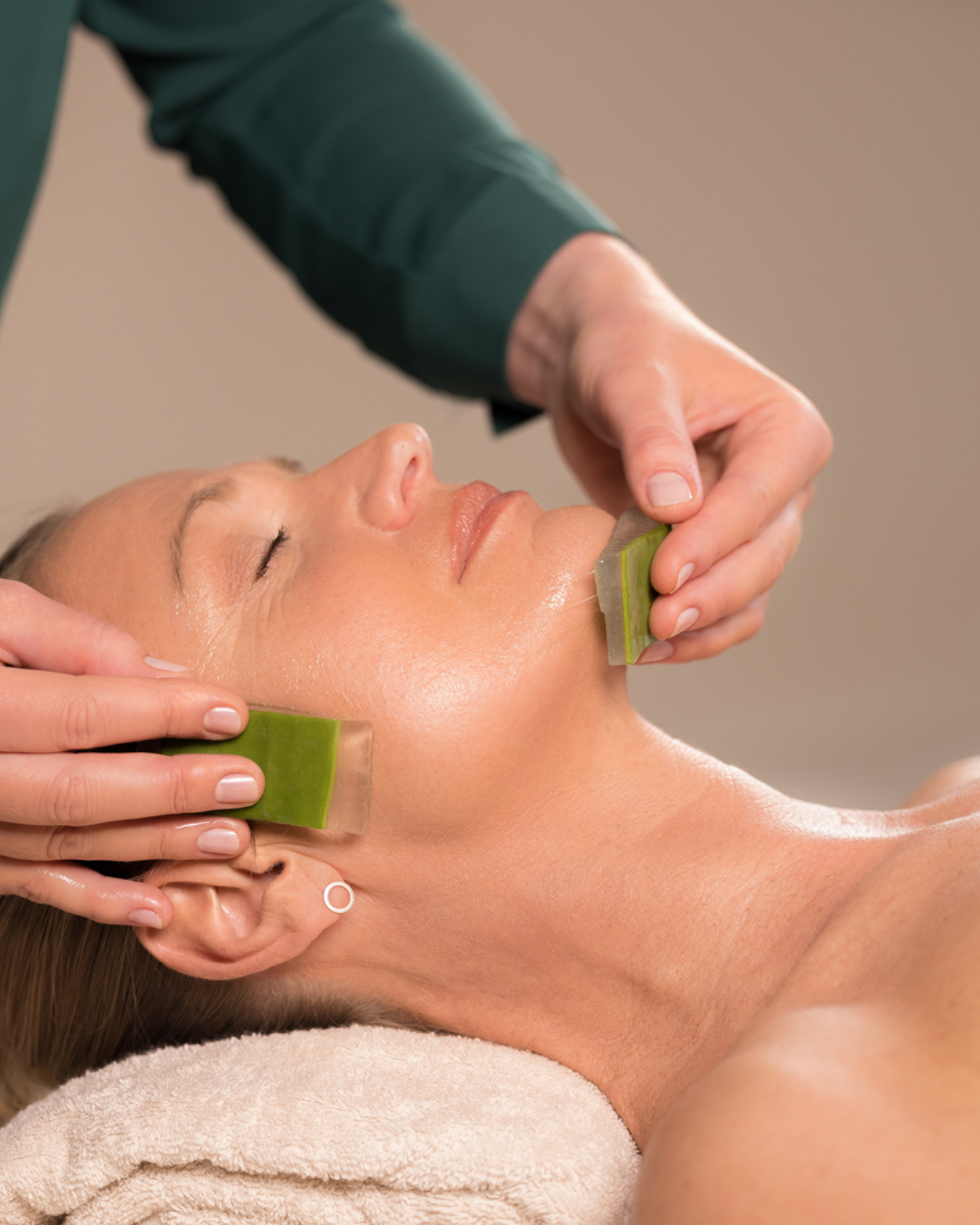 Two flat green stones press against a reclining woman's cheek and jaw.