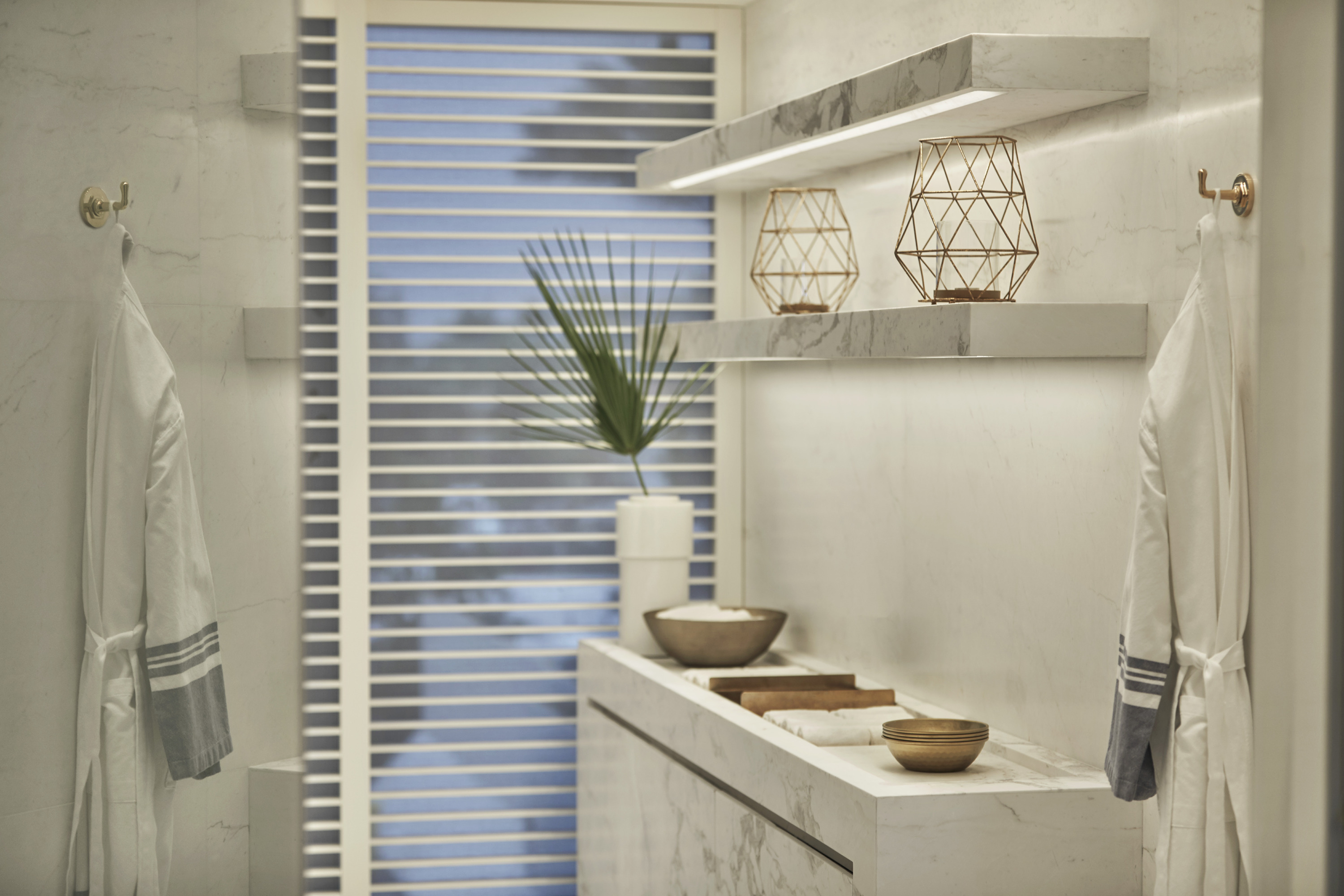 Two white robes with blue-grey striped trim hang beside a marble shelf with wooden bowls and wire lanterns.