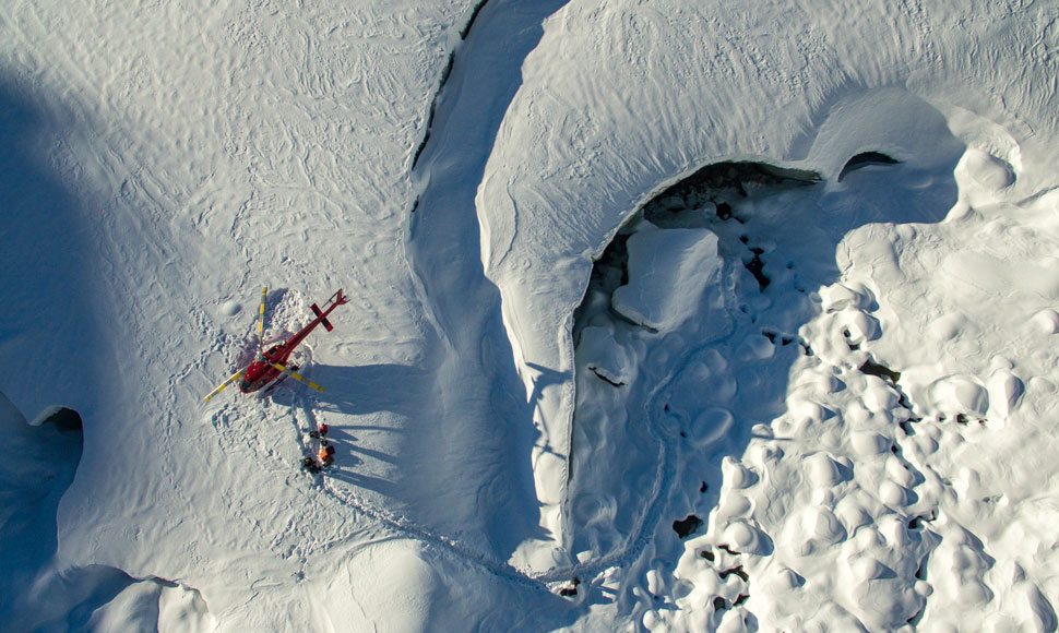 A helicopter landing on a snowy mountaintop in Whistler