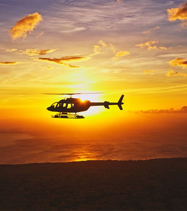 Flying helicopter silhouetted by sunset