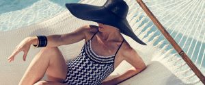 Woman in a black and white abstract print swimsuit and large black sunhat lounges in a hammock