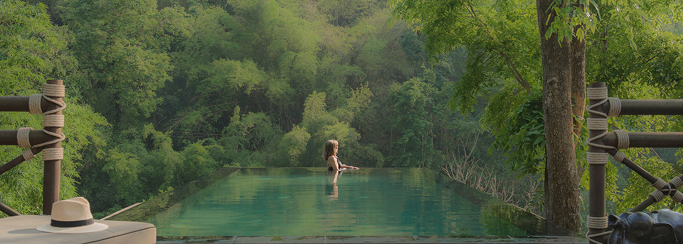 A woman swims in an outdoor pool surrounded by lush, tropical greenery