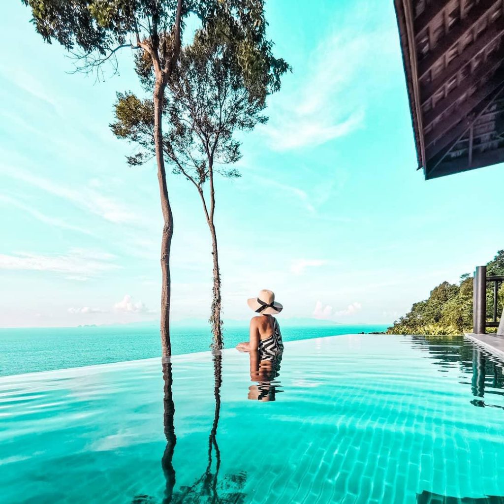 Woman in a wide brim hat lounges on the edge of an infinity pool