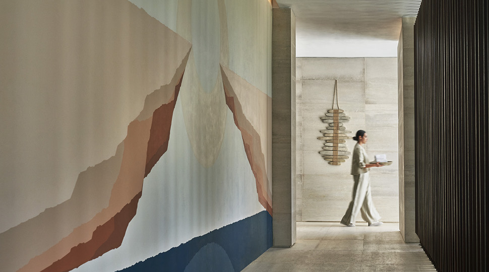 Woman walks through a hallway holding a tray with a mural on the wall