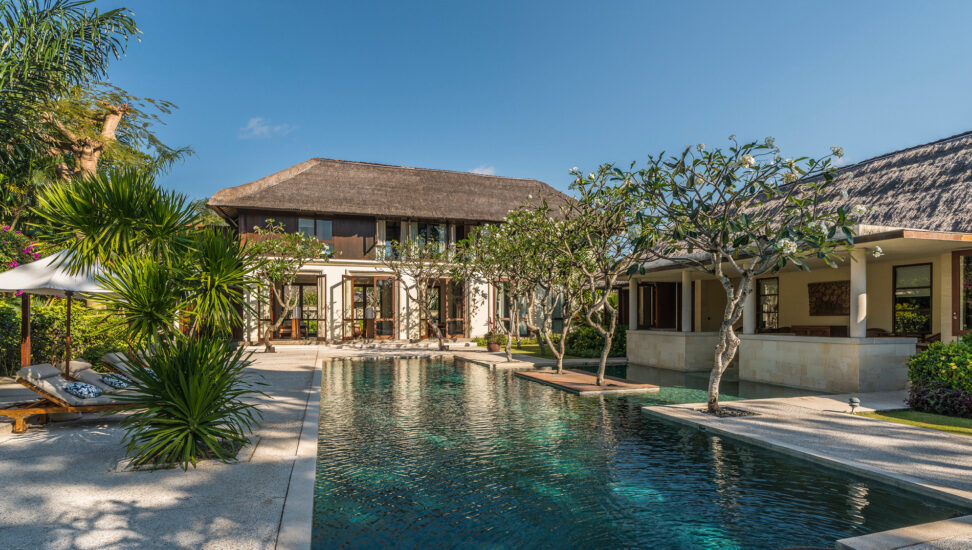 A long private pool and lounge area lined with tropical trees